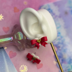 White ear-shaped object with red bow and gold heart on a colorful background