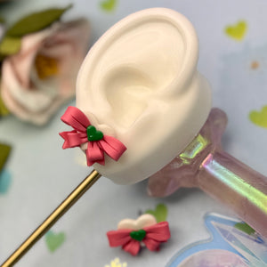 Model of a human ear with a pink bow attached, on a colorful background.